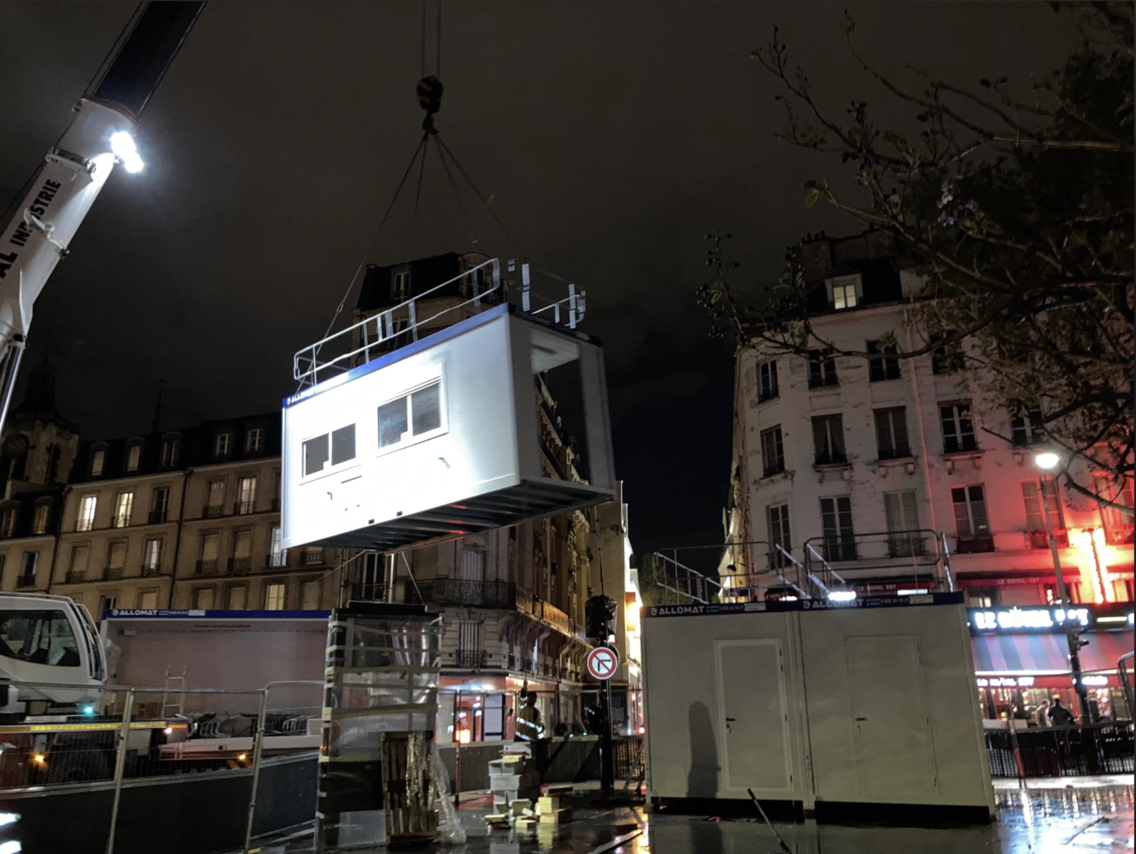 Un module est gruté par-dessus un bâtiment, de nuit.