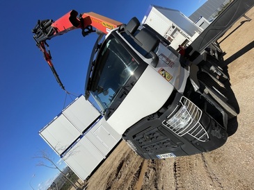 Un camion est en train de gruter un bungalow de chantier Allomat en R+1 pour l'établissement d'une base vie de chantier. Plusieurs autres bungalows sont visibles en arrière-plan sur le chantier.