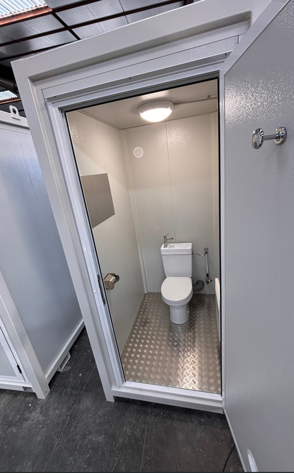 Un module Sanibox d'allomat, avec la porte ouverte. On y voit le WC avec le lavabo intégré et le miroir. Le plancher est en tôle