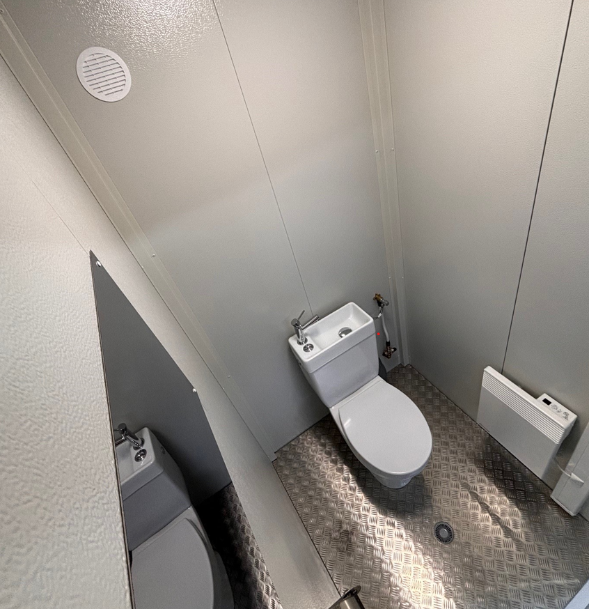 Un module Sanibox d'Allomat, module sanitaire avec un toilette, un lavabo, un panneau électrique en haut à droite et un miroir sur le mur de gauche au-dessus du lavabo.