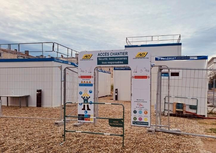 Portique d'accès d'une base vie de chantier sécurisée, entouré de modules Allomat.