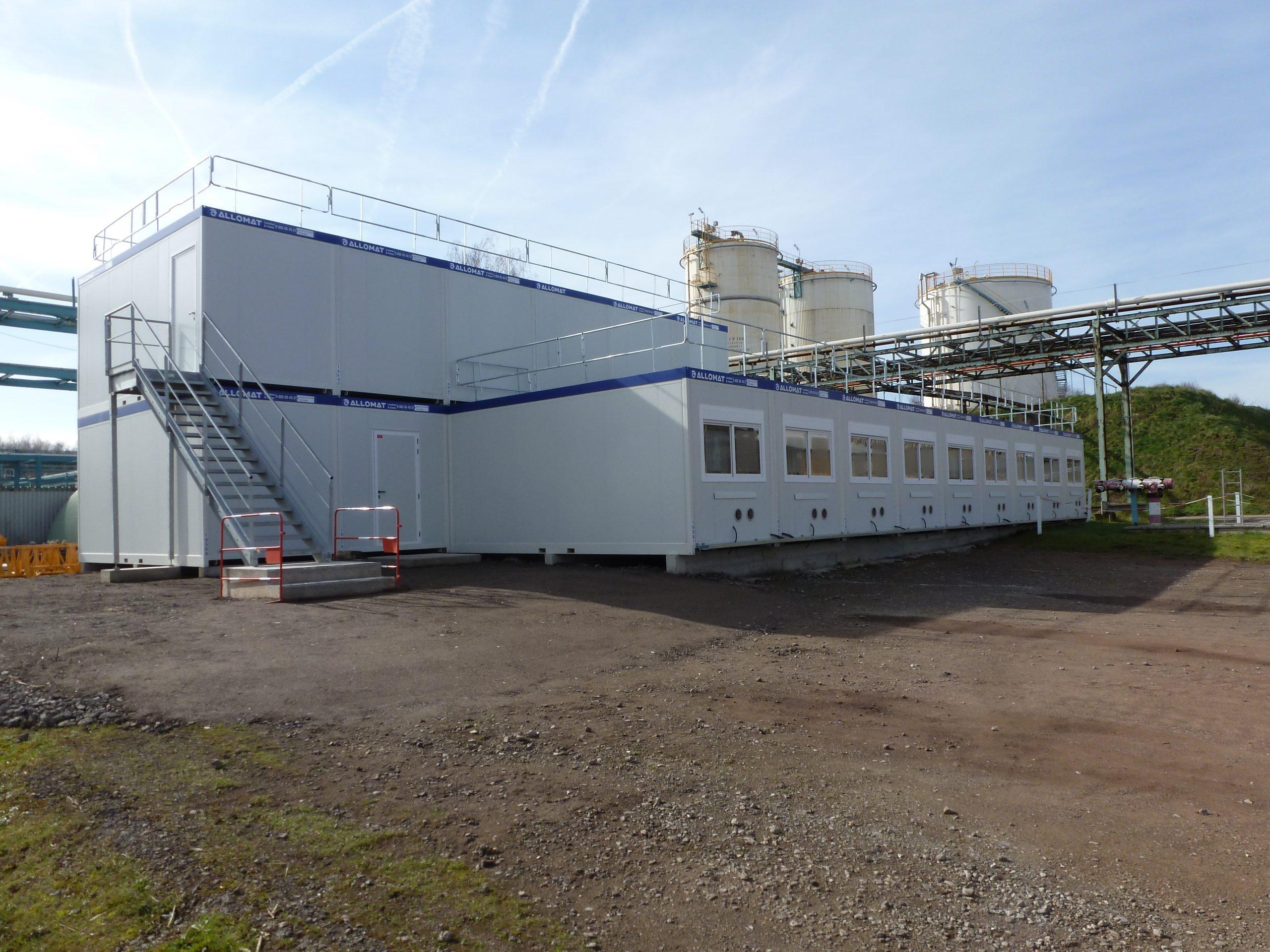 Grande cabane de chantier modulaire Allomat sur deux niveaux, près de réservoirs industriels.