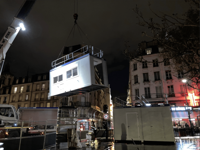 Grue installant un bungalow de chantier Allomat de nuit en milieu urbain.