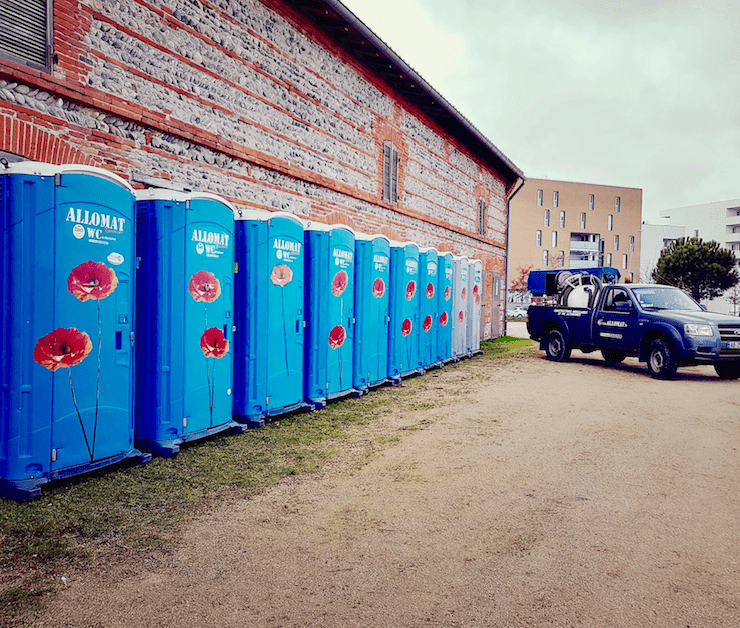 Longue rangée de toilette chimique bleues Allomat avec décoration florale (coquelicots).