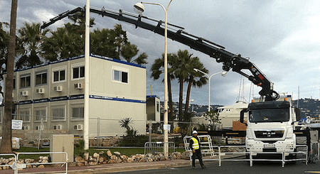 Camion-grue manipulant un bâtiment de bureau modulaire à deux étages. Modules disponibles en occasion.