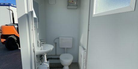 Vue intérieure d'un bloc sanitaire modulaire de chantier avec WC, lavabo et chauffage.