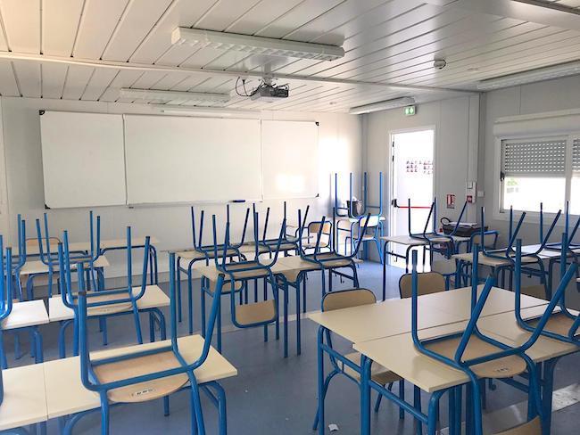 Salle de classe préfabriquée vide avec mobilier, tableau et vidéoprojecteur.