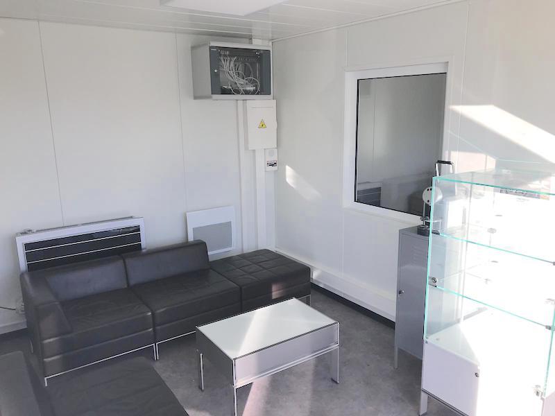 Intérieur de bureau préfabriqué aménagé en salon d'accueil (canapé, vitrine).