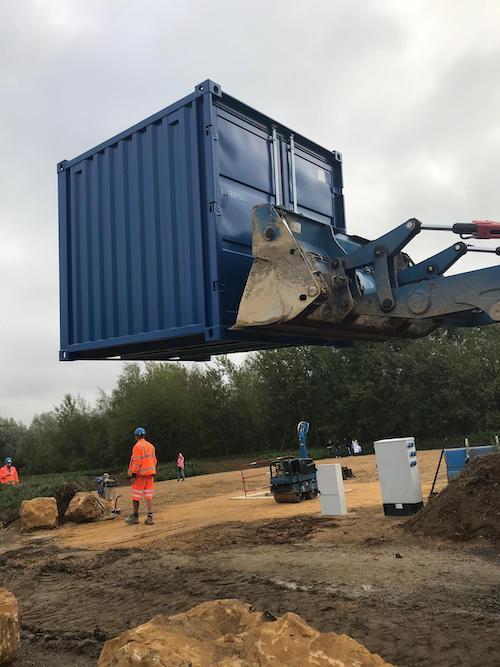 Engin soulevant un conteneur bleu.