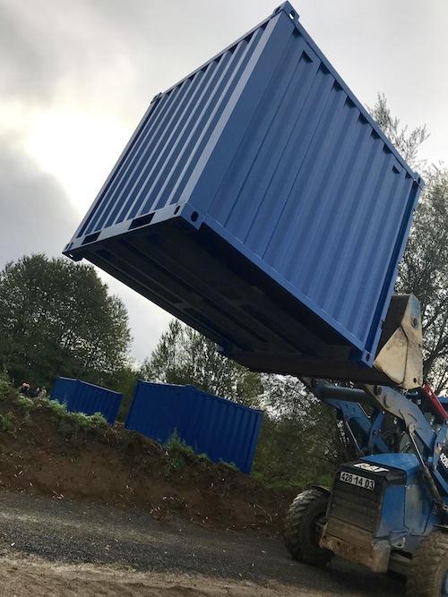 Engin de chantier soulevant un conteneur bleu, illustrant la livraison de conteneur location.