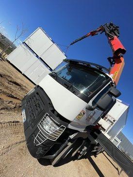 Camion-grue en cours de déchargement d'un module pour location module de chantier.