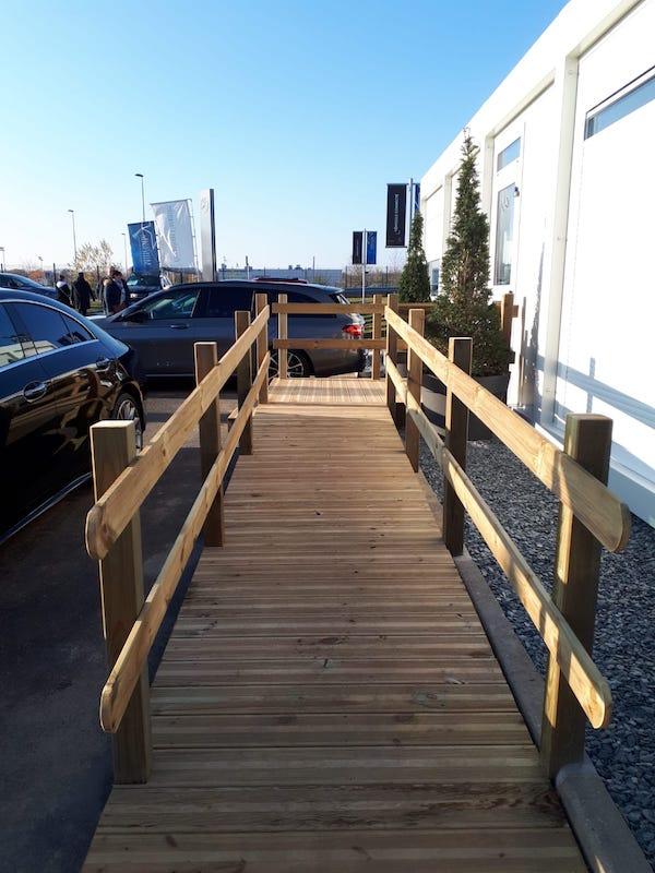 Rampe d'accès en bois avec garde-corps menant à un module de bureau de chantier.